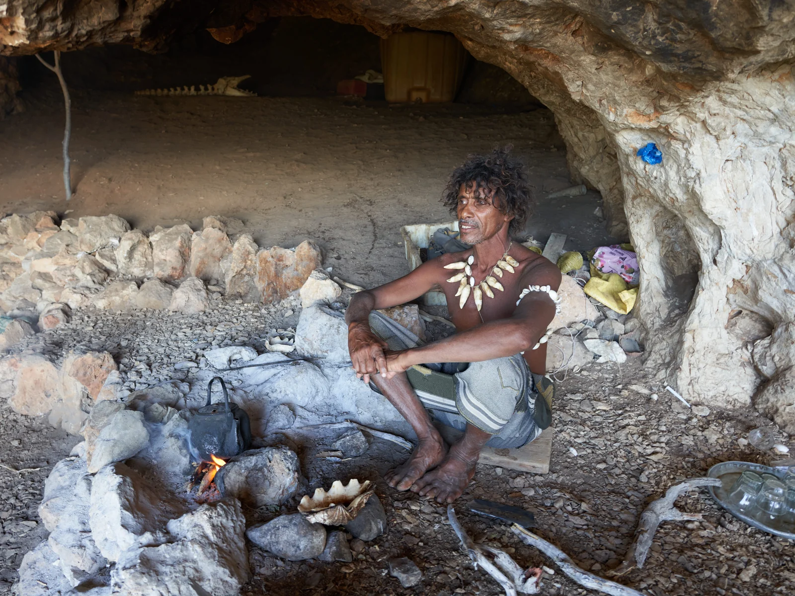 A Socotri man seated beside a small fire inside a rock shelter